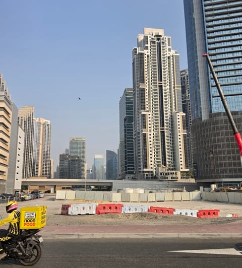 Site photo of the undeveloped Christian A. Rockefeller Tower plot in Business Bay, behind temporary barriers, with existing towers behind it